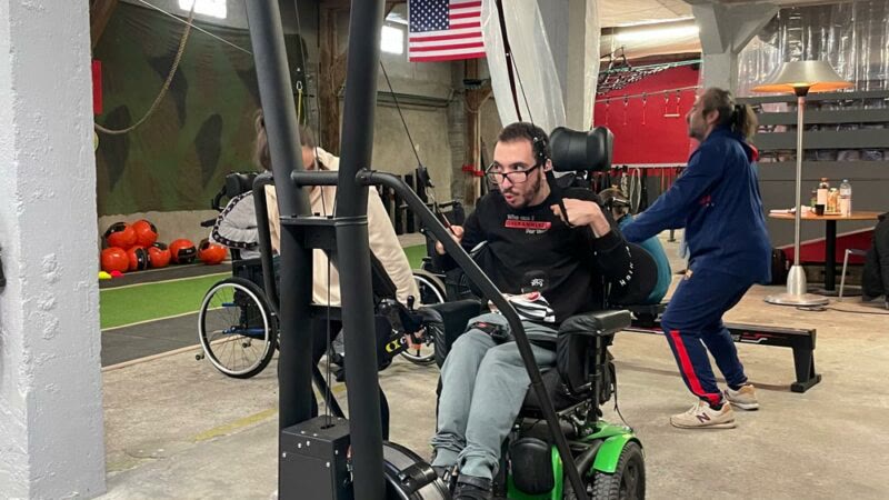 Un adhérent en fauteuil électrique travaille son cardio sur un appareil adapté, dans la salle d'ADAPTATEAM.