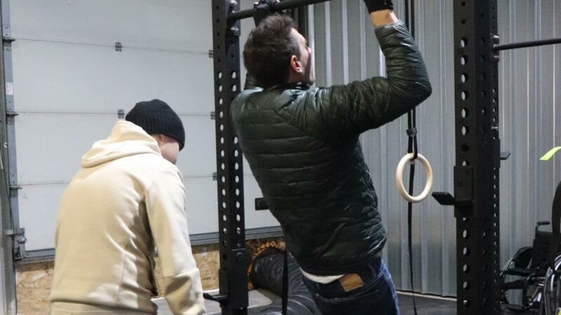 Un adhérent s'entraîne à la barre de traction, son binôme à ses côtés.
